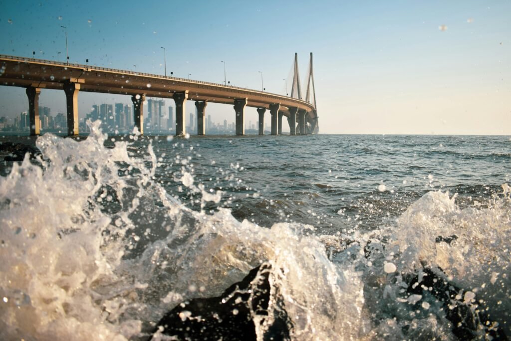 Splashing waves against the Bandra-Worli Sea Link bridge with Mumbai skyline in the background.