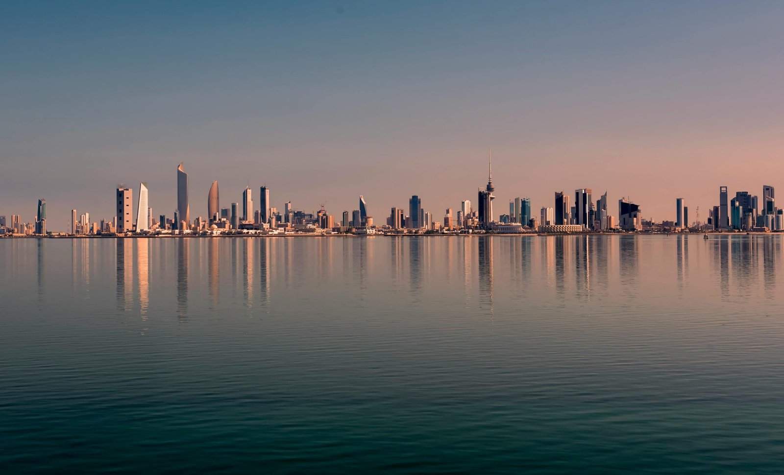 Beautiful Kuwait City skyline reflected on calm water at sunset, showcasing modern architecture.