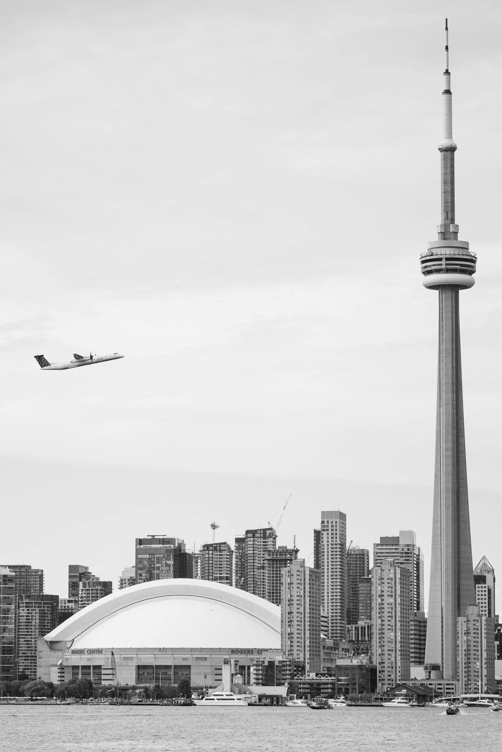 Cheap flights to Canada from London, A stunning black and white view of Toronto's skyline featuring the CN Tower and Rogers Centre with an airplane overhead.