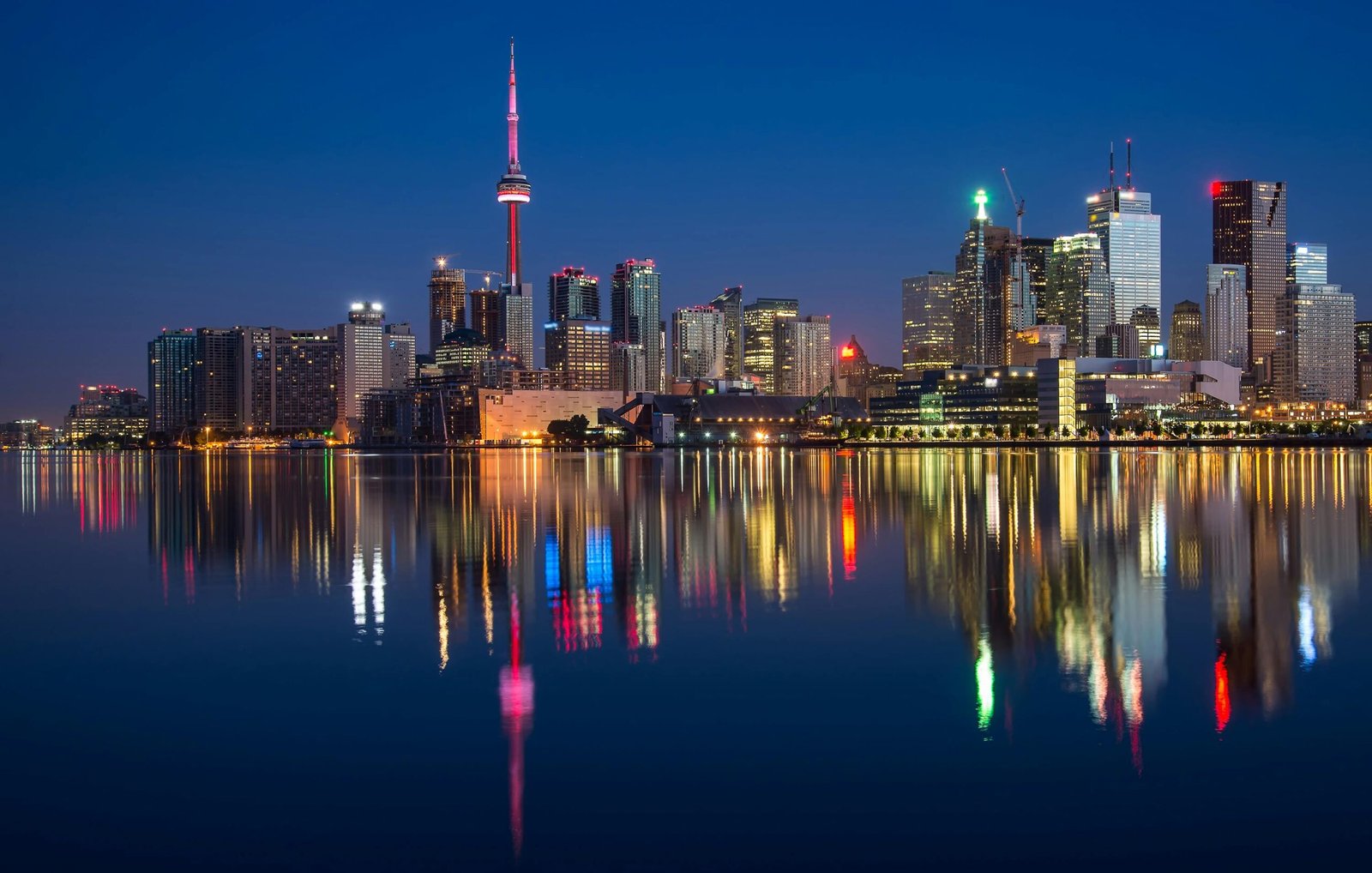 Cheap flights to Canada from London, Stunning night view of Toronto skyline reflecting on water with CN Tower prominent.